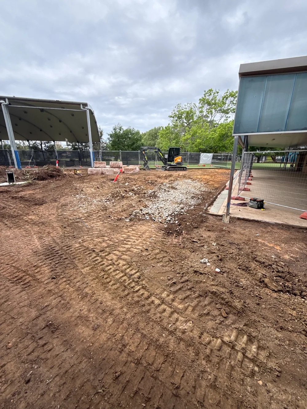 Play area stripped and excavated before the drainage and base works, with an excavator on site