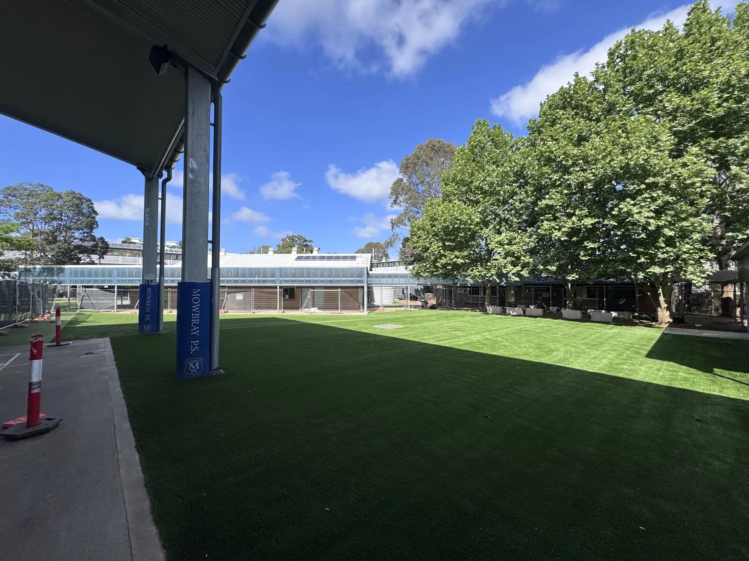 Wide view of the finished synthetic grass from under the covered outdoor area, with Mowbray P.S. post pads and established trees